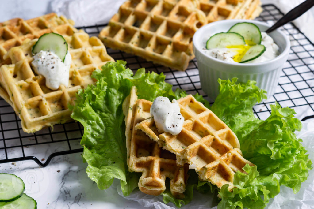 Zucchiniwaffeln mit Zaziki, Salatblättern und Gurkenscheiben angerichtet