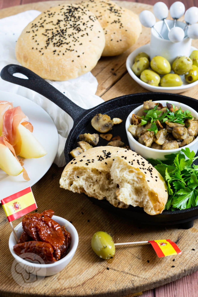 Gebratene Knoblauch Champignons mit Petersilie, Oliven, getrockneten Tomaten und Fladenbrot. Tapas serviert in einer gusseisernen Pfanne.