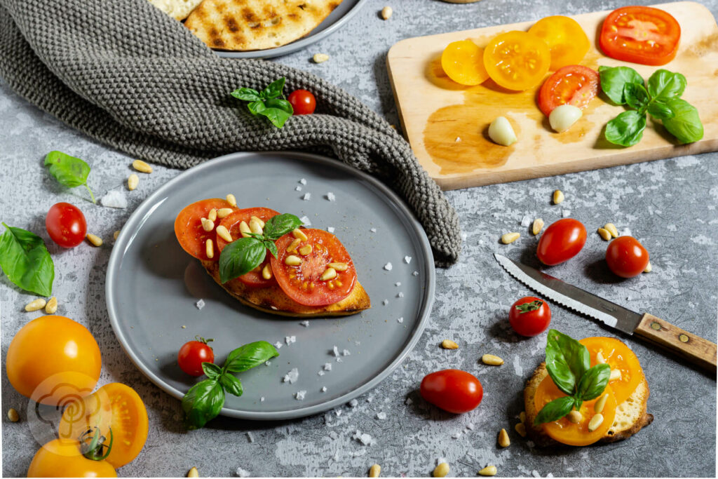Geröstetes Brot mit Tomaten, Pinienkernen und Basilikum auf einem Teller