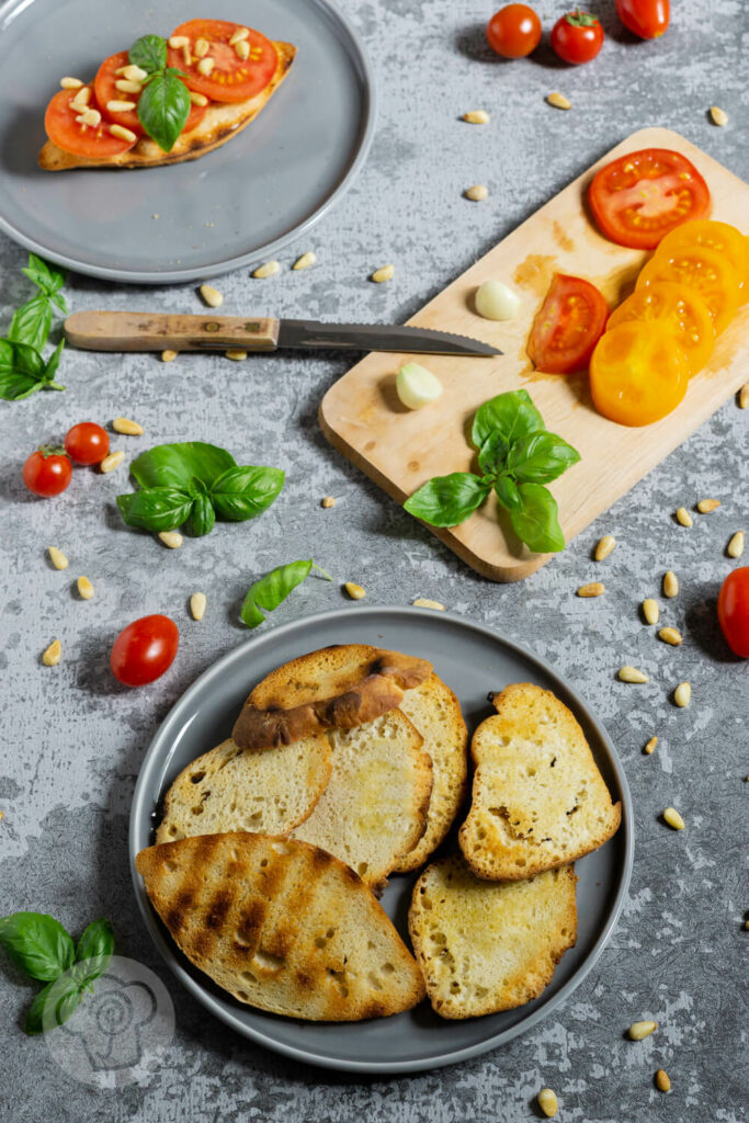 Geröstetes Brot mit Tomaten, Pinienkernen und Basilikum auf einem Teller