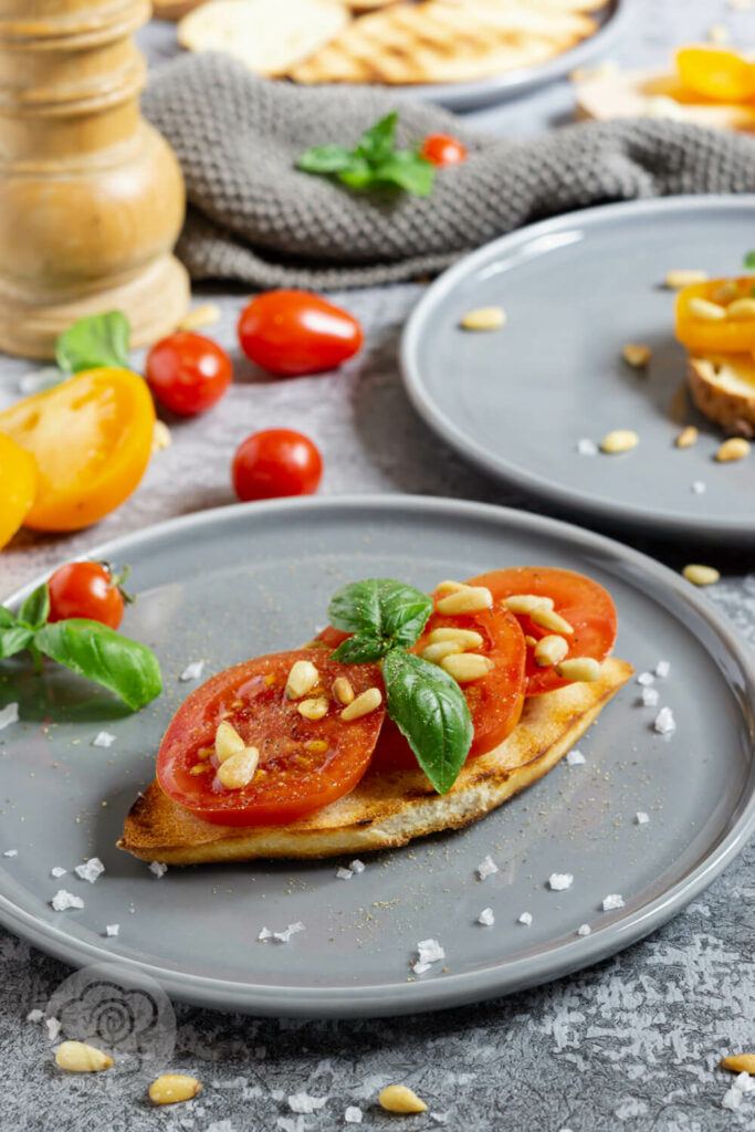 Geröstetes Brot mit Tomaten, Pinienkernen und Basilikum auf einem Teller