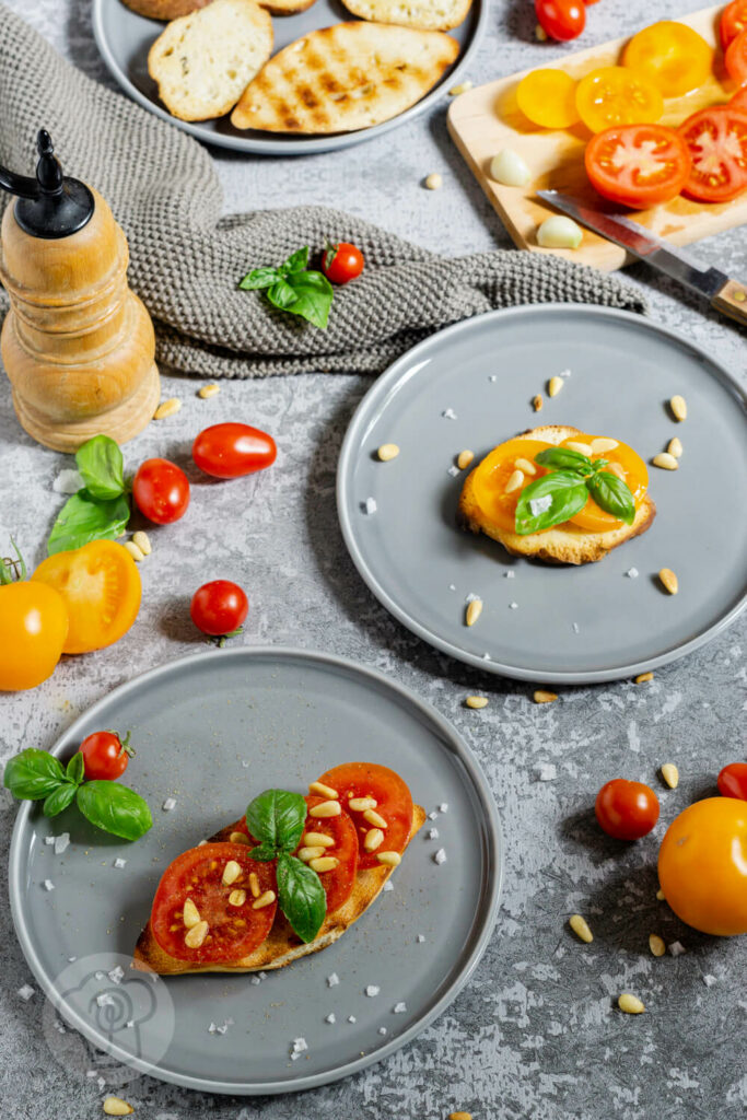 Geröstetes Brot mit Tomaten, Pinienkernen und Basilikum auf einem Teller