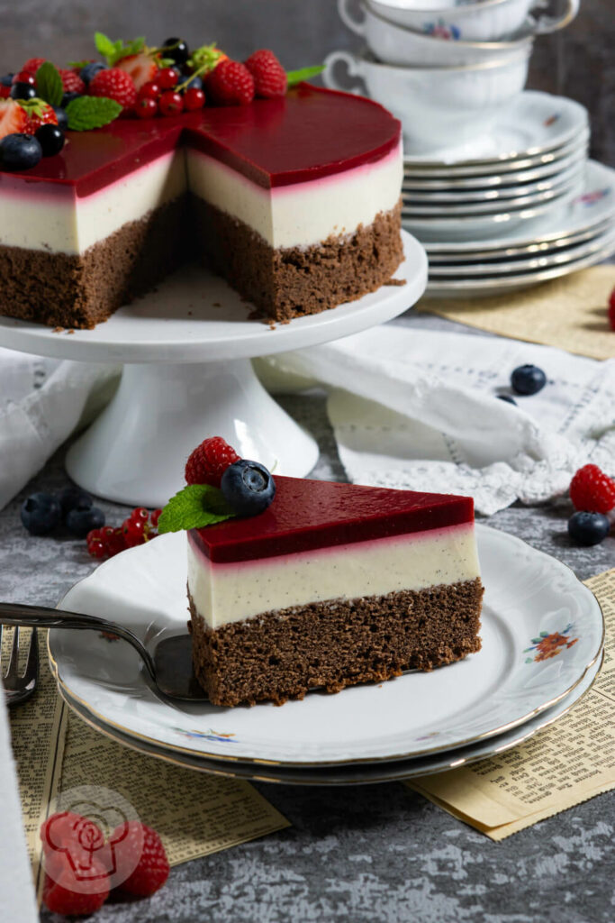 Stück Panna Cotta Torte auf einem Teller. Restliche Torte und Kaffeegeschirr im Hintergrund