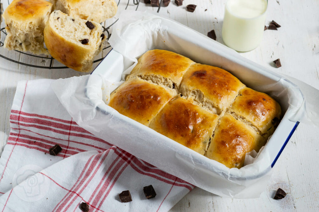 Dänische Schokobrötchen aus Hefeteig auf einem Rost. Im Hintergrund eine Flasche Milch und noch mehr Brötchen.