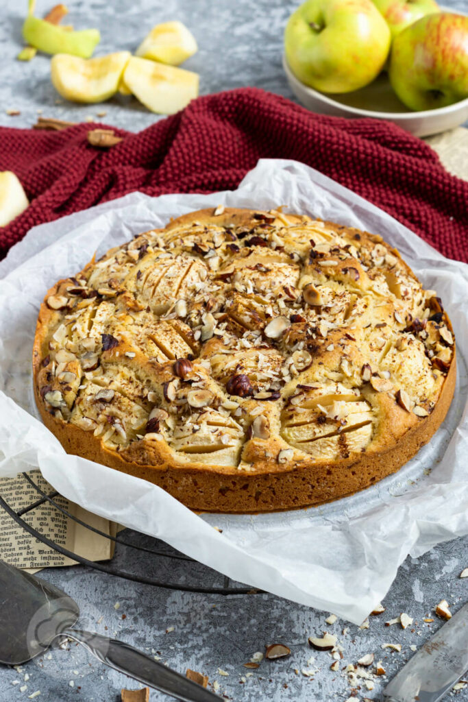 Einfacher gedeckter Apfelkuchen mit Nüssen. Kuchen auf dem Rost. Äpfel im Hintergrund.