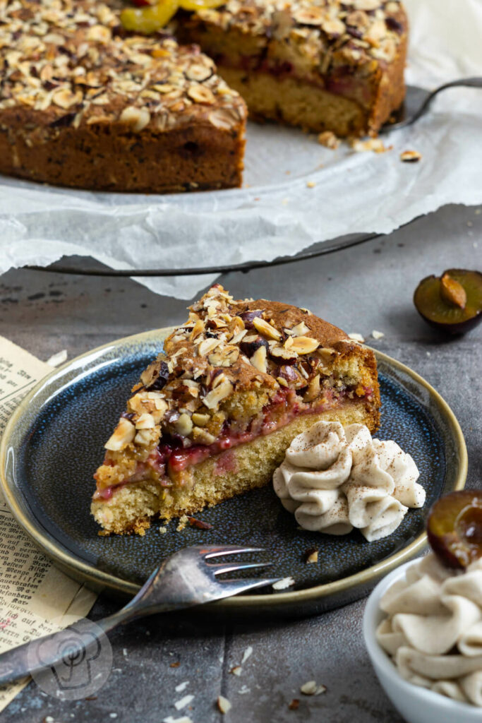 Pflaumenkuchen auf dem Rost im Hintergrund. Ein Stück auf dem Teller im Vordergrund mit Sahne.