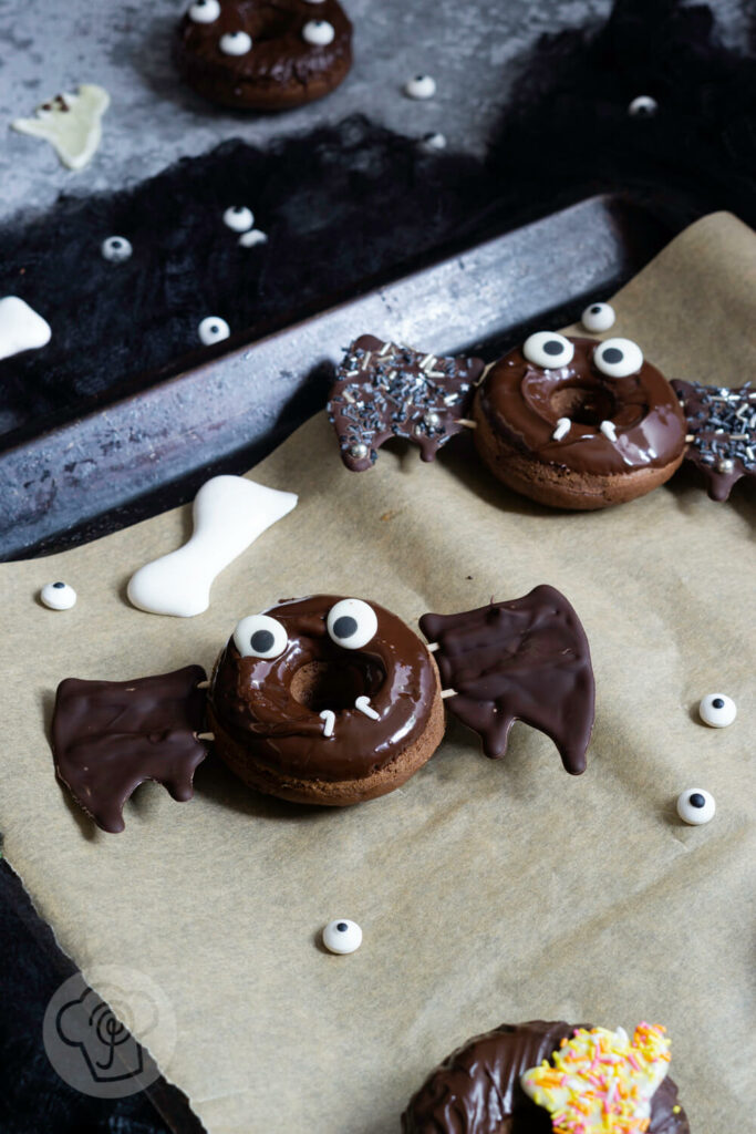 Halloween Donuts mit Schokolade auf einem Blech. Zuckeraugen außenrum.