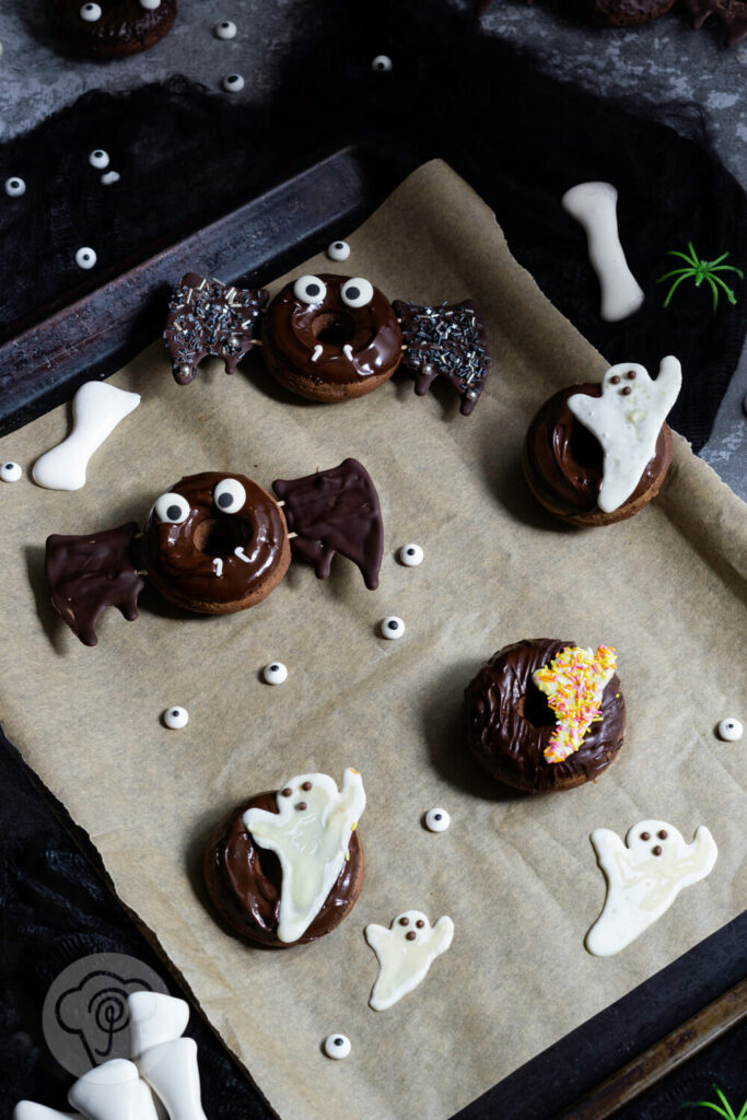 Halloween Donuts mit Schokolade auf einem Blech. Zuckeraugen außenrum.