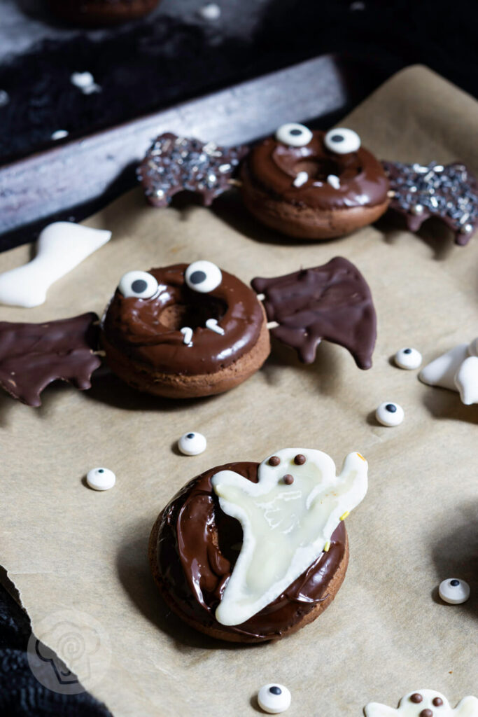 Halloween Donuts mit Schokolade auf einem Blech. Zuckeraugen außenrum.
