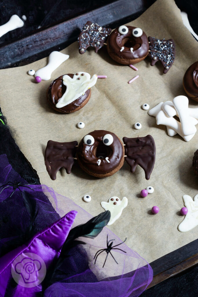 Halloween Donuts mit Schokolade auf einem Blech. Zuckeraugen außenrum.