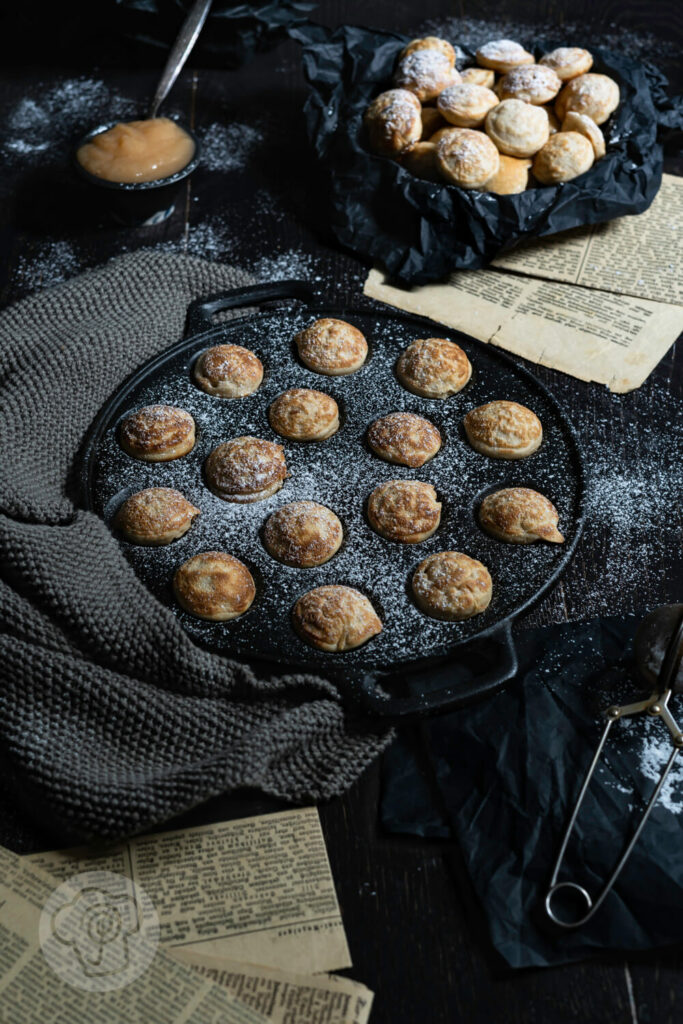 Poffertjes in der Pfanne mit Puderzucker und Apfelbrei.