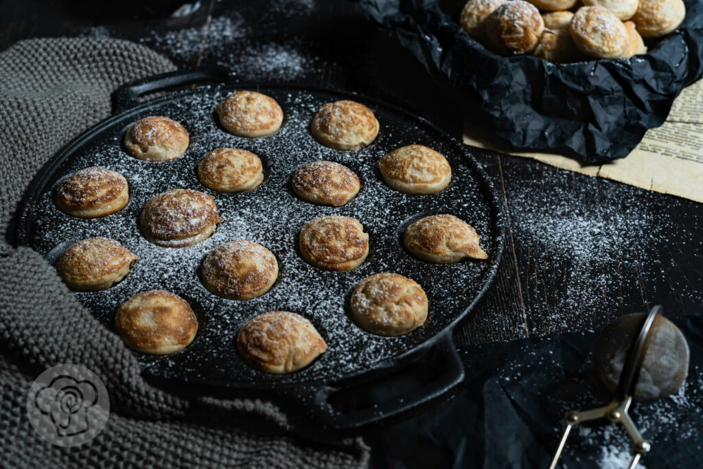 Poffertjes in der Pfanne mit Puderzucker und Apfelbrei.