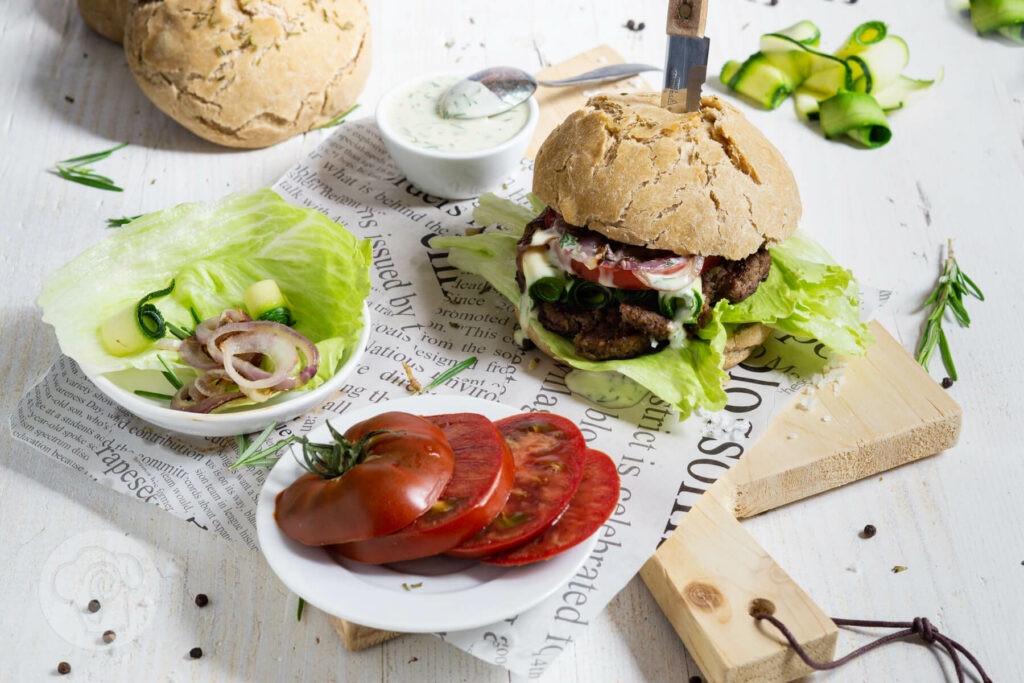 Zwiebel Burger mit Joghurt Mayonnaise mit Tomatenscheiben und Salat auf einem Brett serviert