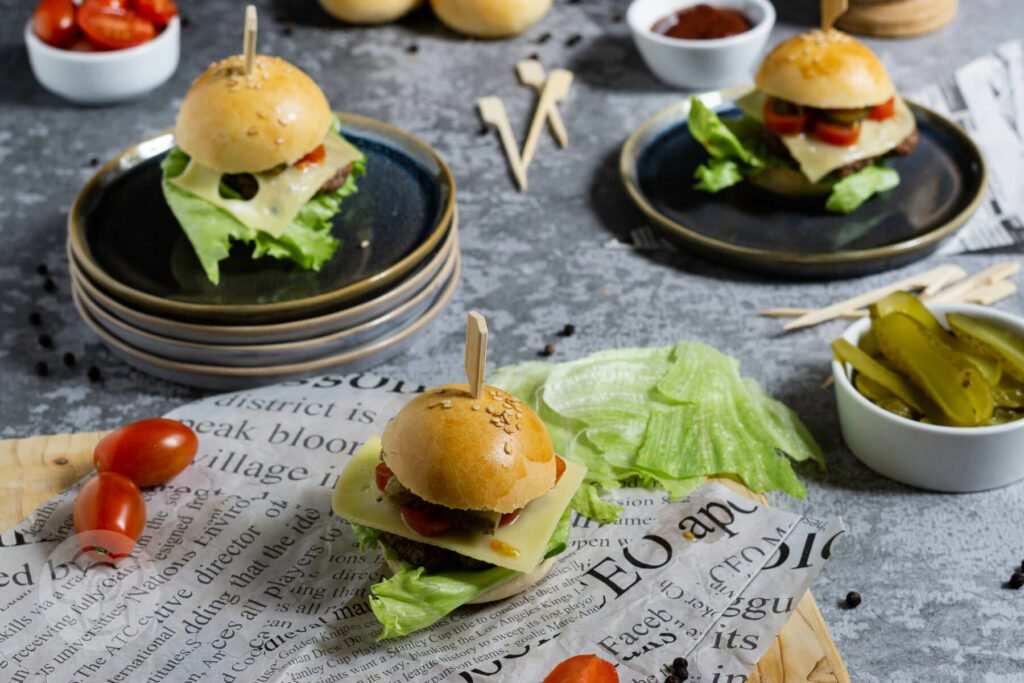Mini Burger auf Tellern verteilt. Dazu Tomaten und Gurken