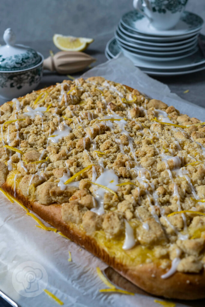 Zitronen Streuselkuchen. Geschirr und Zitronen im Hintergrund.