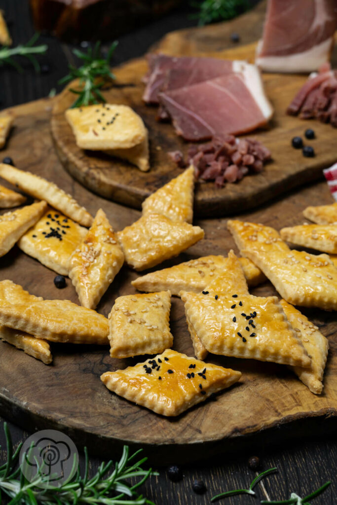 Cracker mit Schwarzwälder Schinken auf einem Brett. Dazu Wacholderbeeren, Schinkenstreifen und Rosmarin.