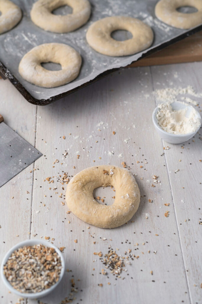 Bagels ungebacken auf einem Blech im Hintergrund. Ein Bagel im Vordergrund.