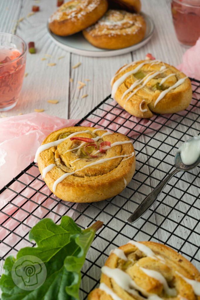 Marzipanschnecken mit Rhabarber und Zuckerguss auf einem Rost. Im Hintergrund Rhabarberlimonade.