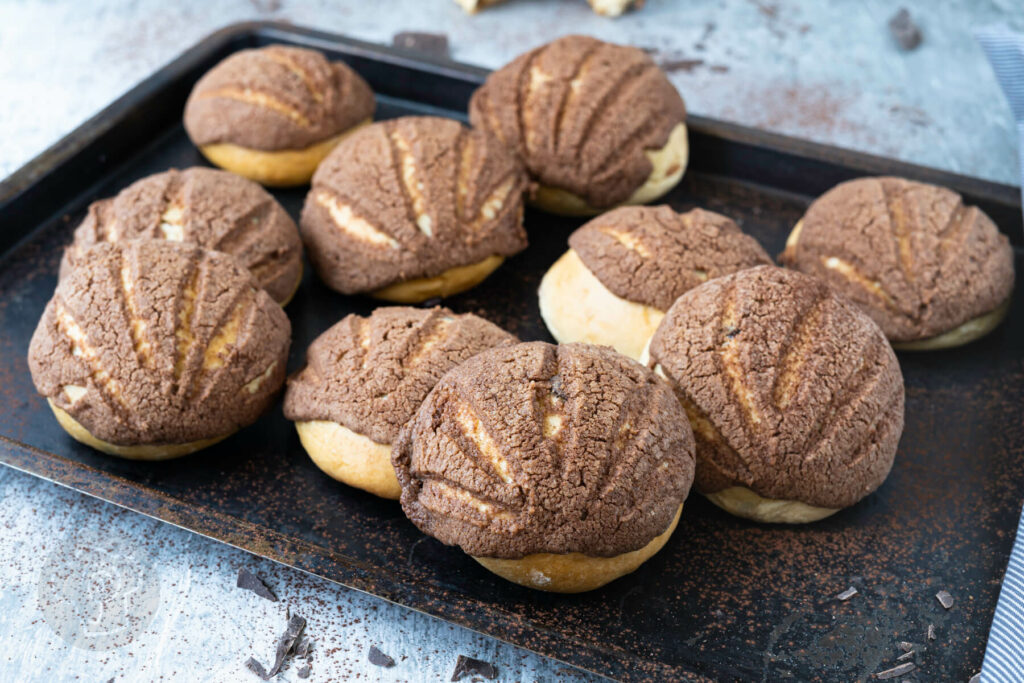 Mexikanische Conchas auf einem Blech mit Schokostückchen.