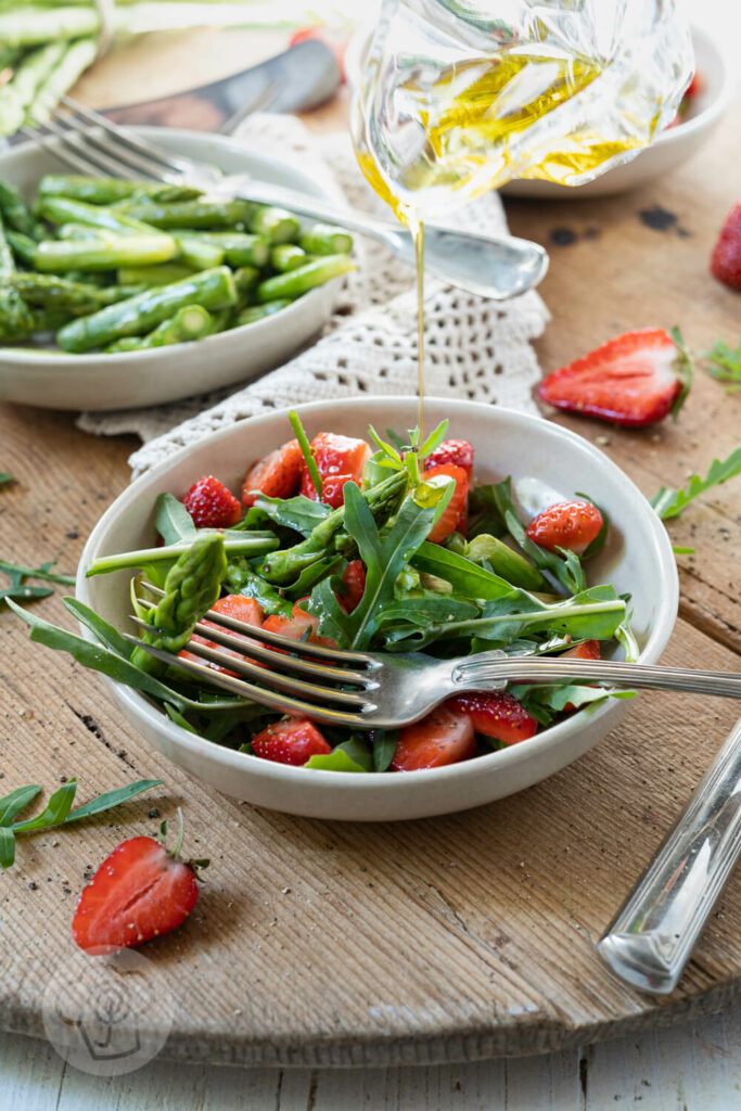 Spargelsalat mit grünem Spargel, Erdbeeren und Rucola in kleinen Tellern.