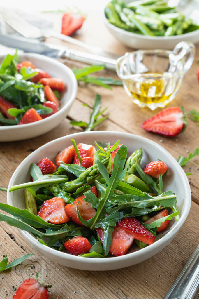 Spargelsalat mit grünem Spargel, Erdbeeren und Rucola in kleinen Tellern.