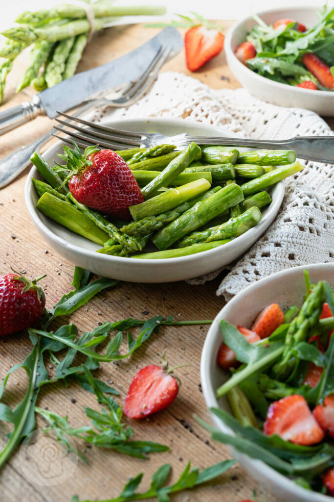 Spargelsalat mit grünem Spargel, Erdbeeren und Rucola in kleinen Tellern.