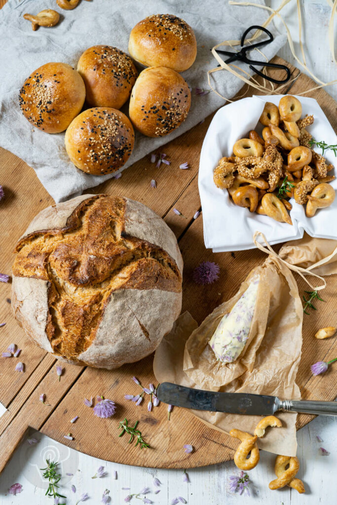 Auffrischbrot für Sauerteigreste auf einem großen Brett, dazu Schnittlauchbutter, Brioche Burger Buns und Taralli Pugliesi.