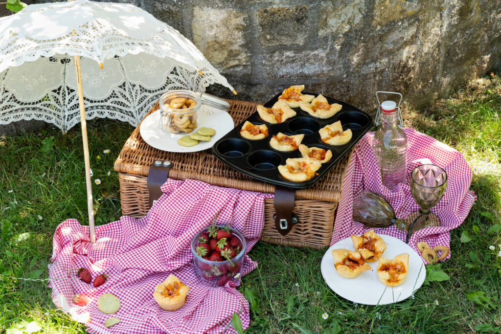 Einfache Pizzamuffins im Muffinblech auf einem Picknickkorb, Sonnenschirm, Picknickdecke, Erdbeeren