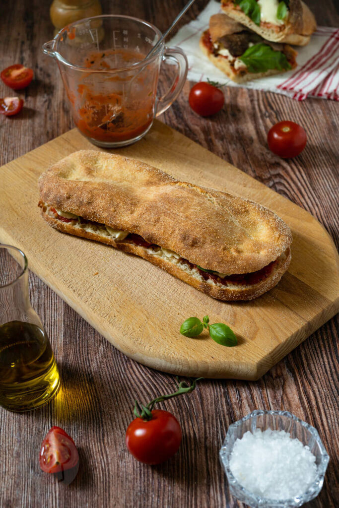 Panuozzo napoletano auf einem Holzbrett. Im Hintergrund ein Brot aufgeschnitten.