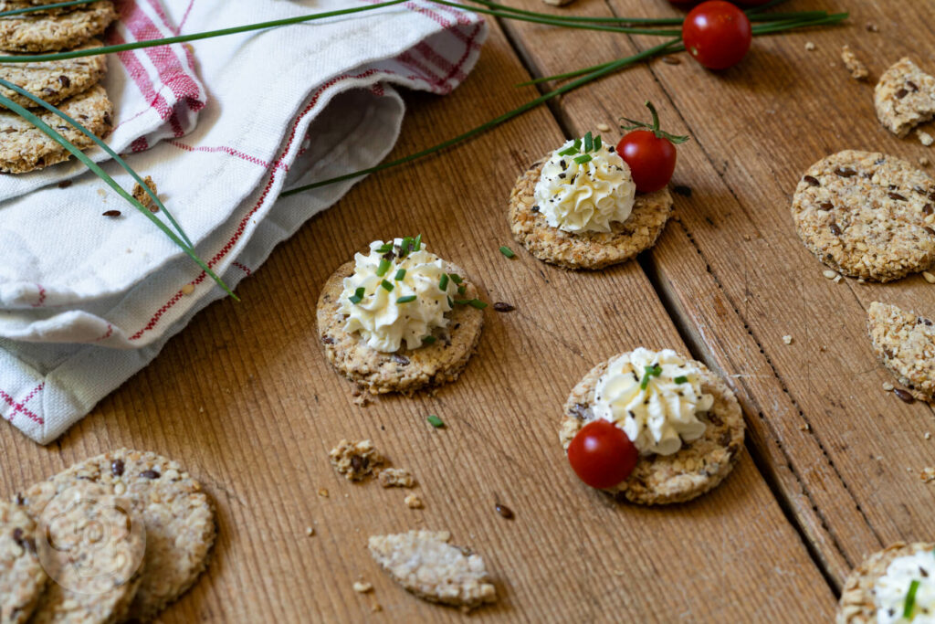 Schnelle Cracker auf einem Brett. Teilweise mit einer Frischkäsecreme und Tomaten.