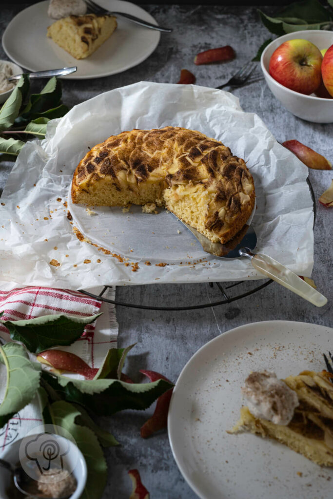 Schwedischer Apfelkuchen auf einem Rost, angeschnitten. Dazu Teller mit Kuchenstücken