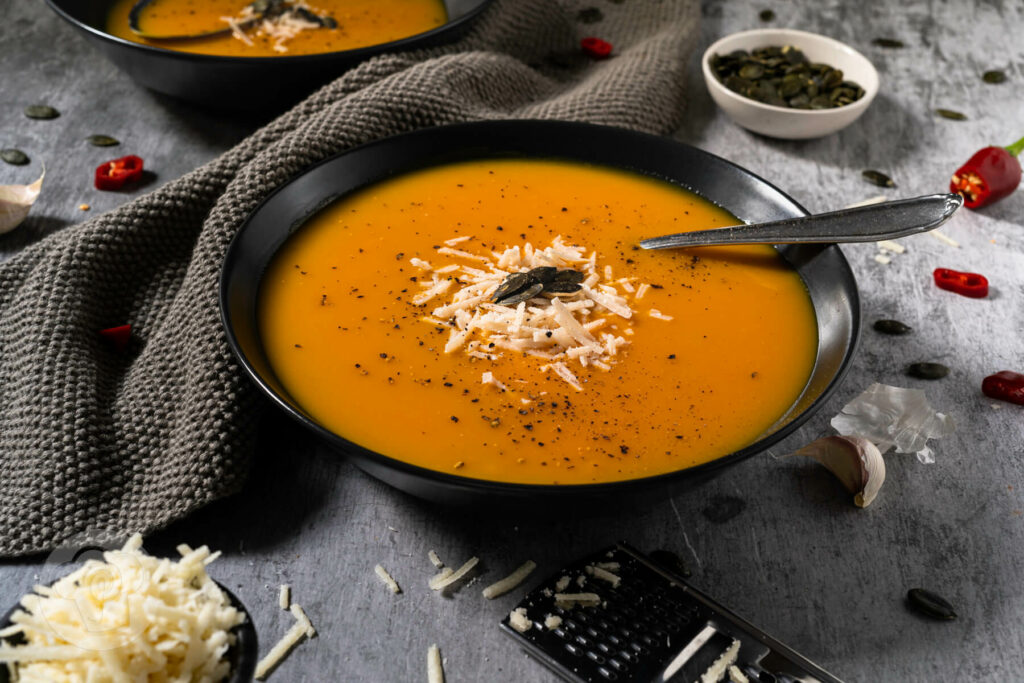Brasilianische Kürbissuppe in zwei tiefen Tellern. Serviert mit Kürbiskernen und Parmesan.