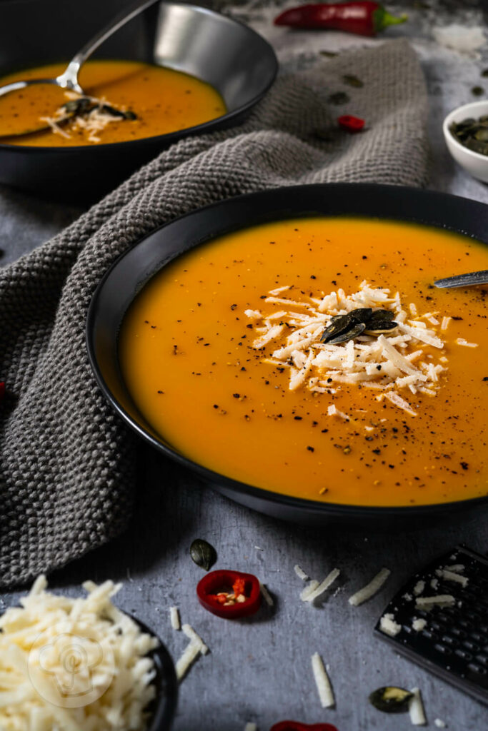 Brasilianische Kürbissuppe in zwei tiefen Tellern. Serviert mit Kürbiskernen und Parmesan.