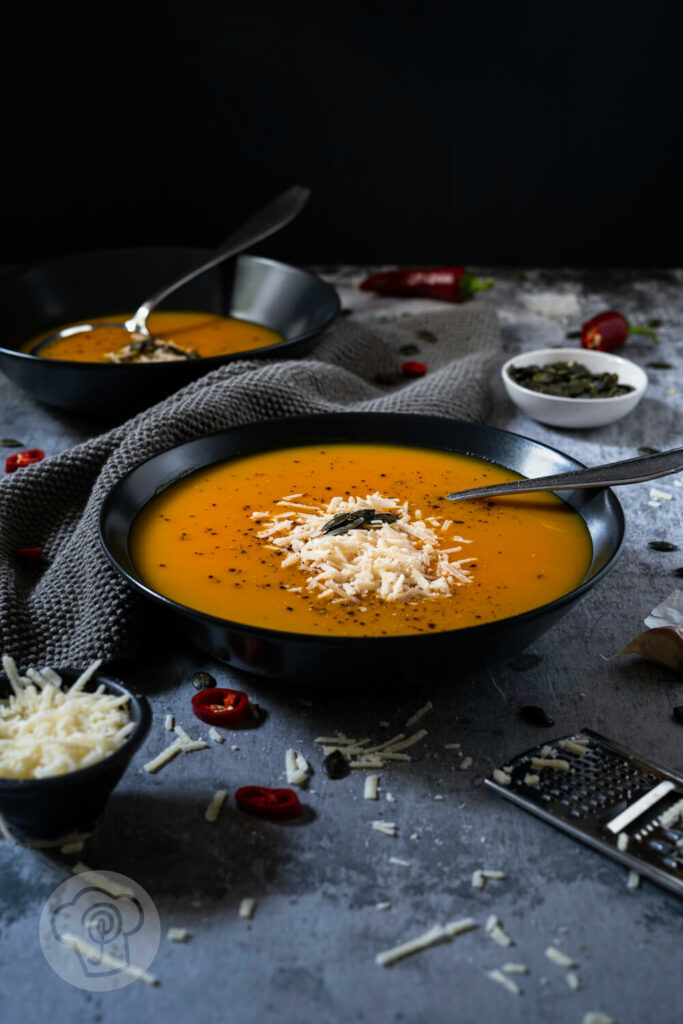 Brasilianische Kürbissuppe in zwei tiefen Tellern. Serviert mit Kürbiskernen und Parmesan.