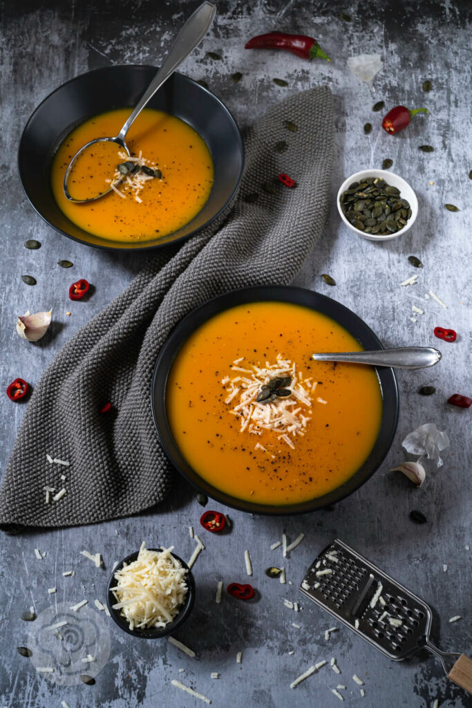 Brasilianische Kürbissuppe in zwei tiefen Tellern. Serviert mit Kürbiskernen und Parmesan.