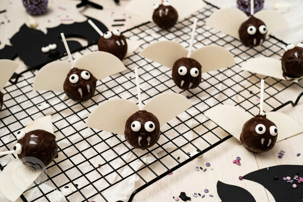 Fledermaus Cake Pops auf einem Gitter. Drum herum Zuckerstreusel, Zuckeraugen und Fledermäuse.