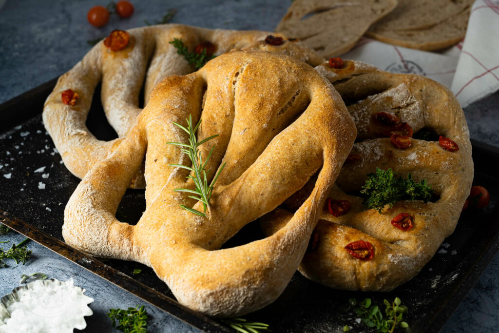 Französische Fougasse auf einem Backblech, mit einem Rosmarinzweig und Tomaten.