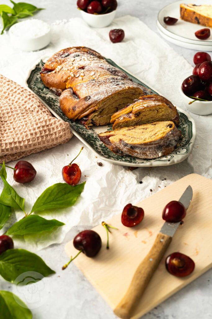 Hefezopf mit Kirschen und Schokostückchen auf einer Kuchenplatte, angeschnitten