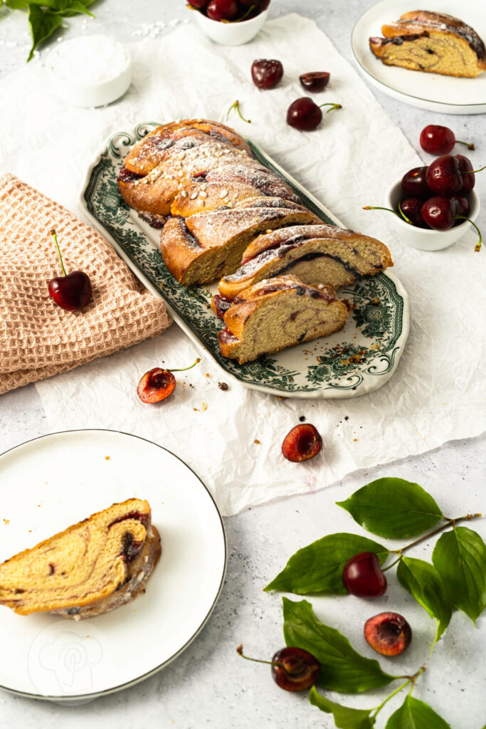 Hefezopf mit Kirschen und Schokostückchen auf einer Kuchenplatte, angeschnitten