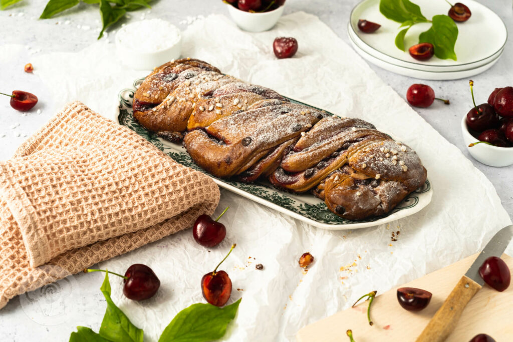 Hefezopf mit Kirschen und Schokostückchen auf einer Kuchenplatte