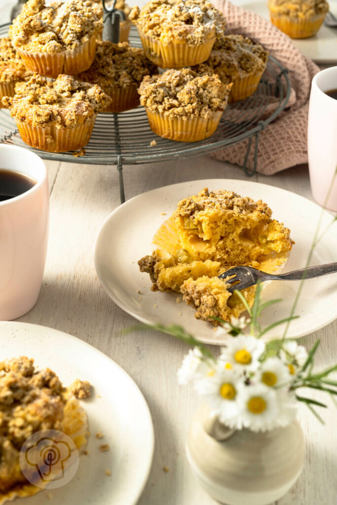 Rhabarbermuffins mit Kardamom Streuseln auf einem Kuchengitter und Teller mit Kaffee