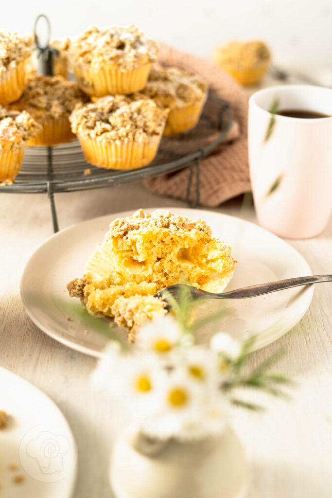 Rhabarbermuffins mit Kardamom Streuseln auf einem Kuchengitter und Teller mit Kaffee