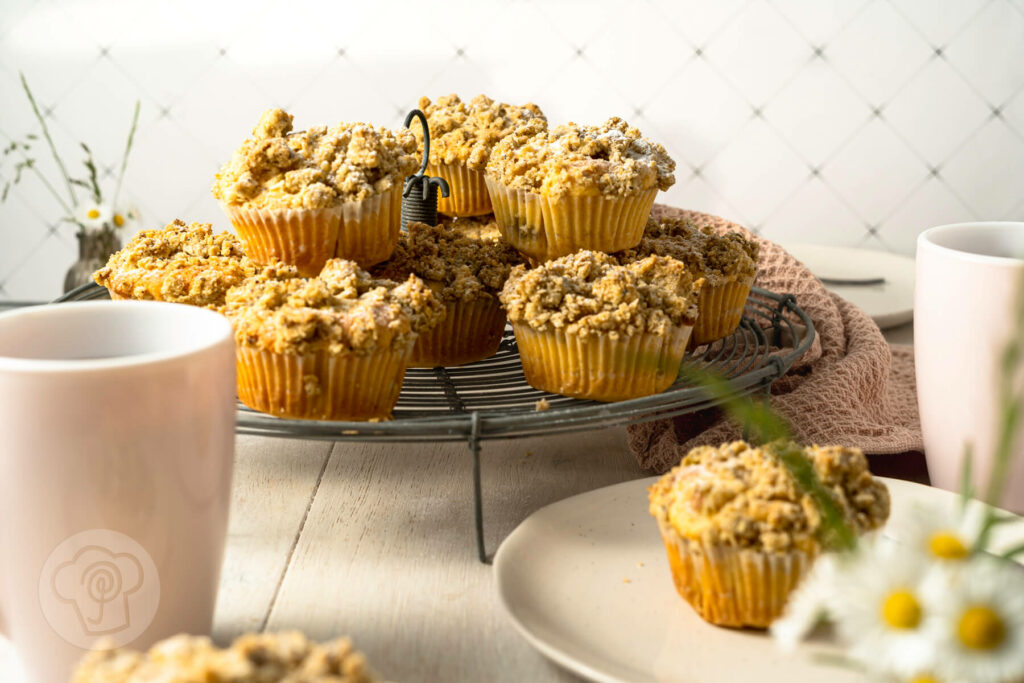 Rhabarbermuffins mit Kardamom Streuseln auf einem Kuchengitter und Teller mit Kaffee