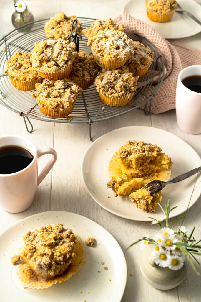 Rhabarbermuffins mit Kardamom Streuseln auf einem Kuchengitter und Teller mit Kaffee