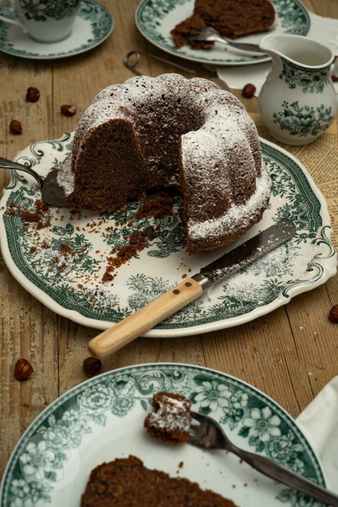 Saftiger Nuss-Gugelhupf mit Lebkuchengewürz angeschnitten auf einer Kuchenplatte. Zwei Stücke auf Tellern.