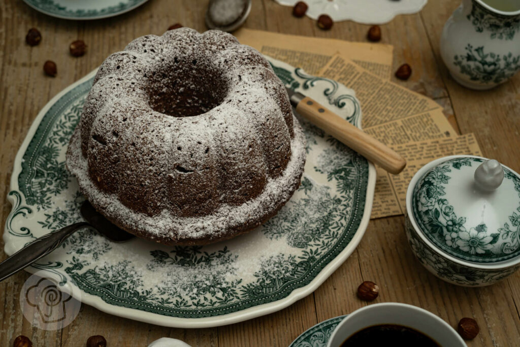 Nuss-Gugelhupf saftig mit Lebkuchengewürz und Puderzucker auf einer Kuchenplatte.