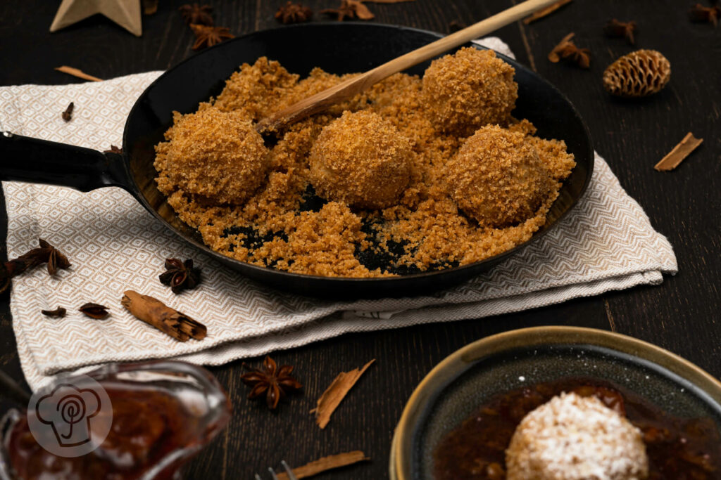 Topfenknödel auf einem Teller und in der Pfanne mit Butterbröseln. Dazu Gewürzpflaumen.